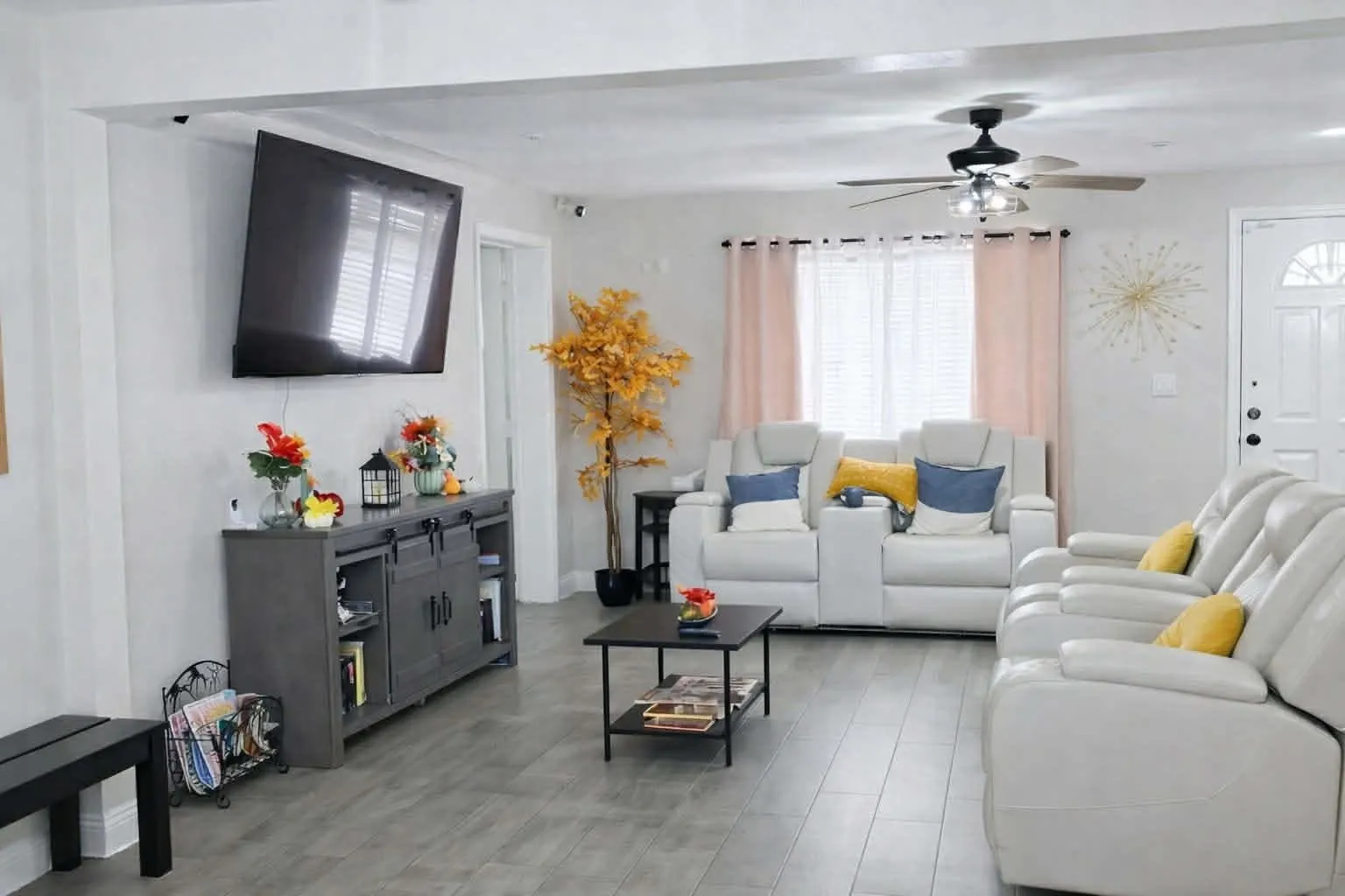 The open living room at Latham, with cream reclining sofas, blue and yellow cushions, and a wall-mounted television