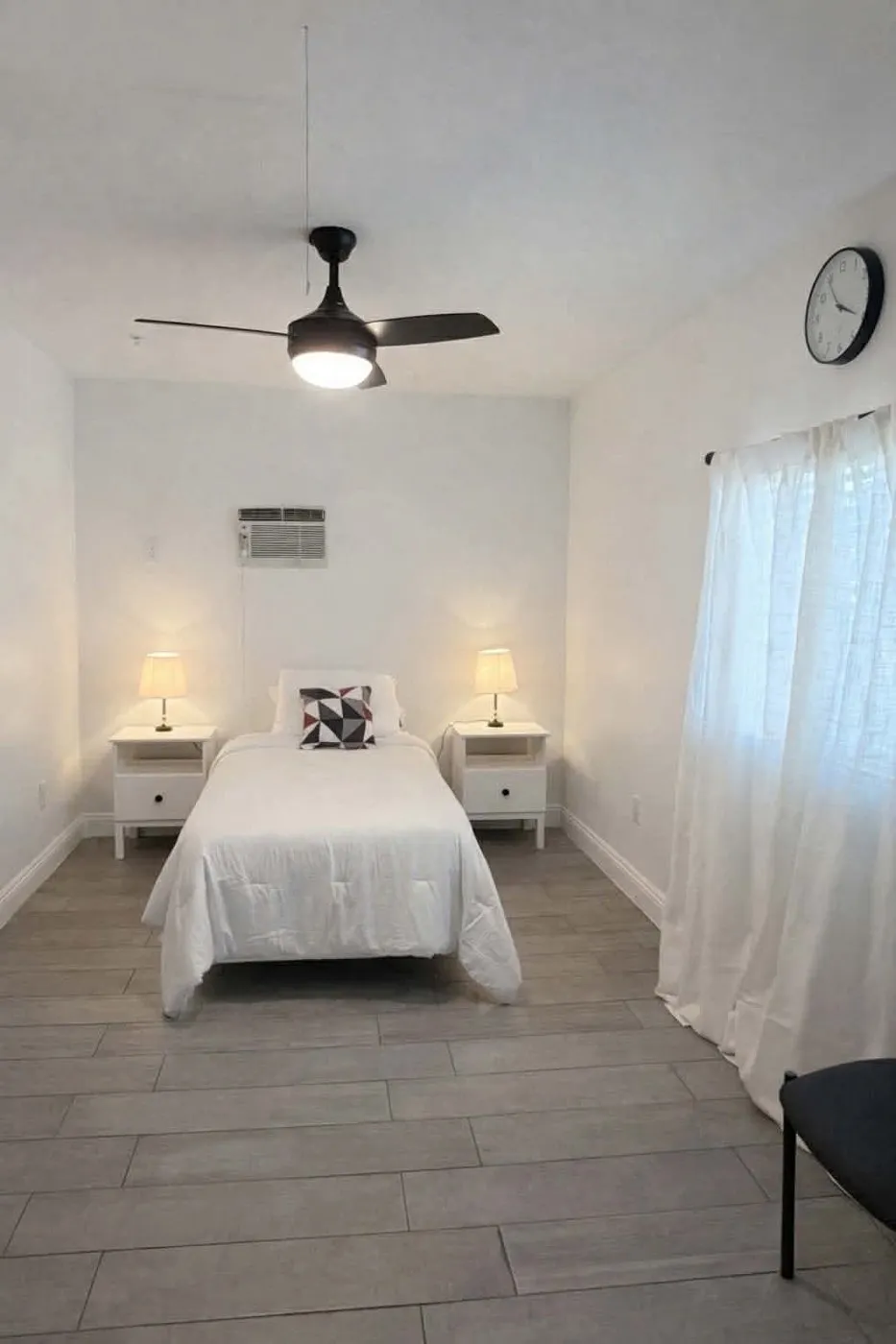 A private resident bedroom at Latham with a single bed, a bedside lamp on each side, and a large curtained window